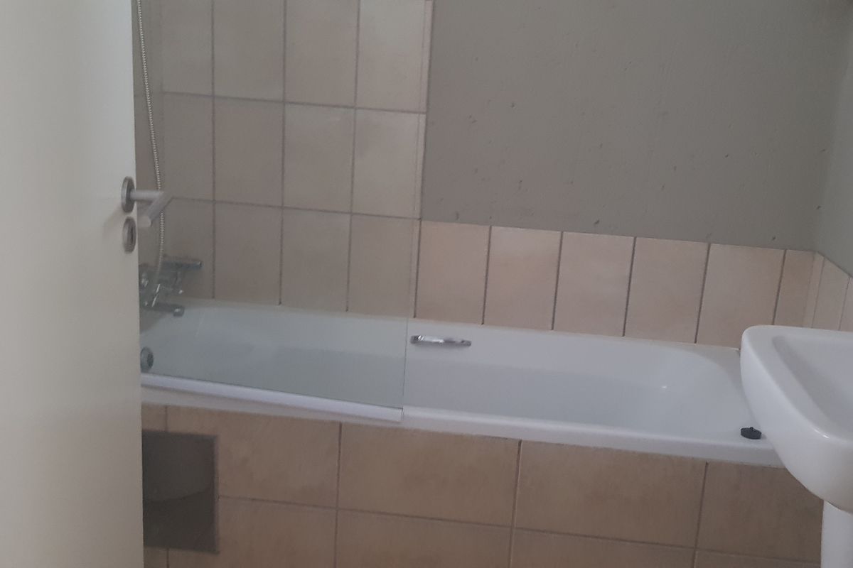 A functional bathroom featuring a standard bathtub with shower mixer and a pedestal basin, requiring cosmetic updates to improve its overall aesthetic appeal.