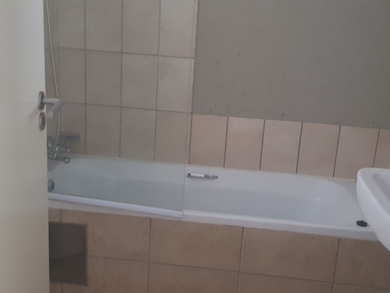 A functional bathroom featuring a standard bathtub with shower mixer and a pedestal basin, requiring cosmetic updates to improve its overall aesthetic appeal.