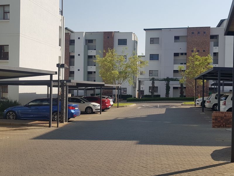 Exterior view of a modern apartment complex featuring paved parking areas with covered bays and multi-story residential buildings.
