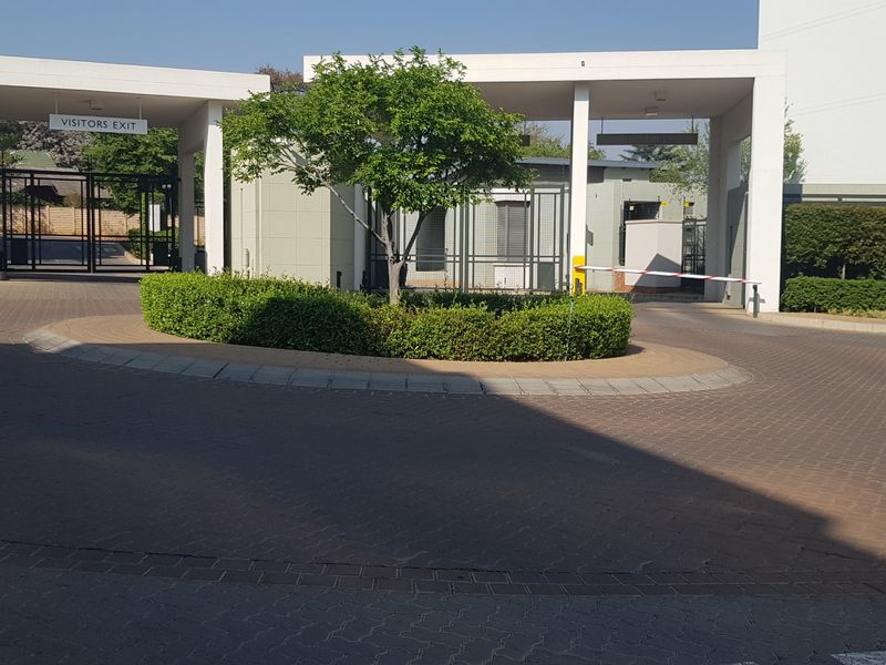 The apartment complex features a secure gated entrance with a paved driveway, boom gate access, and a well-maintained landscaped garden area.