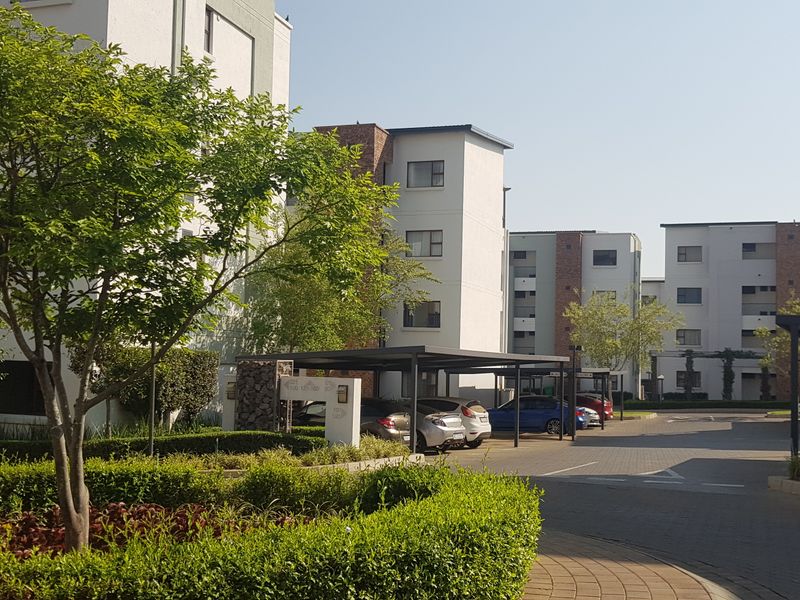 A view of the apartment complex exterior featuring paved driveways, covered parking carports, and well-maintained landscaped garden areas.