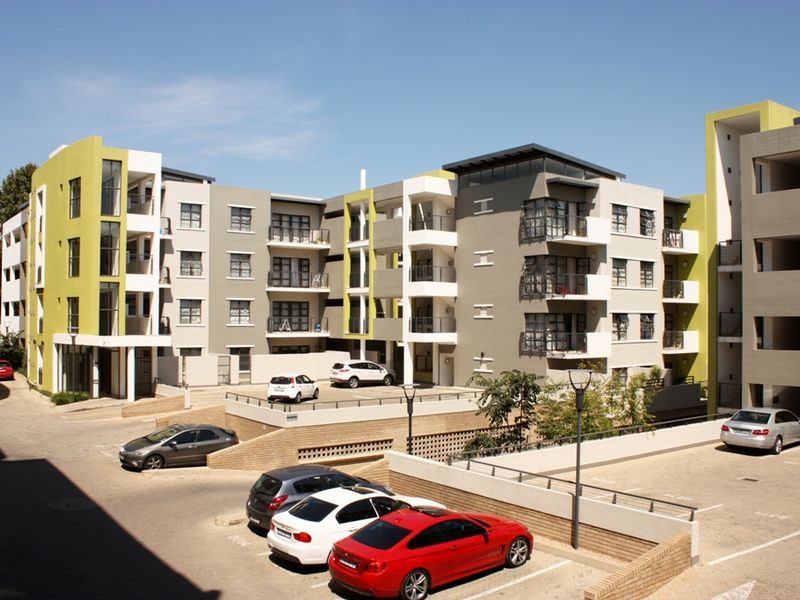 A modern multi-story apartment complex featuring contemporary architectural design, private balconies, and dedicated paved parking facilities.