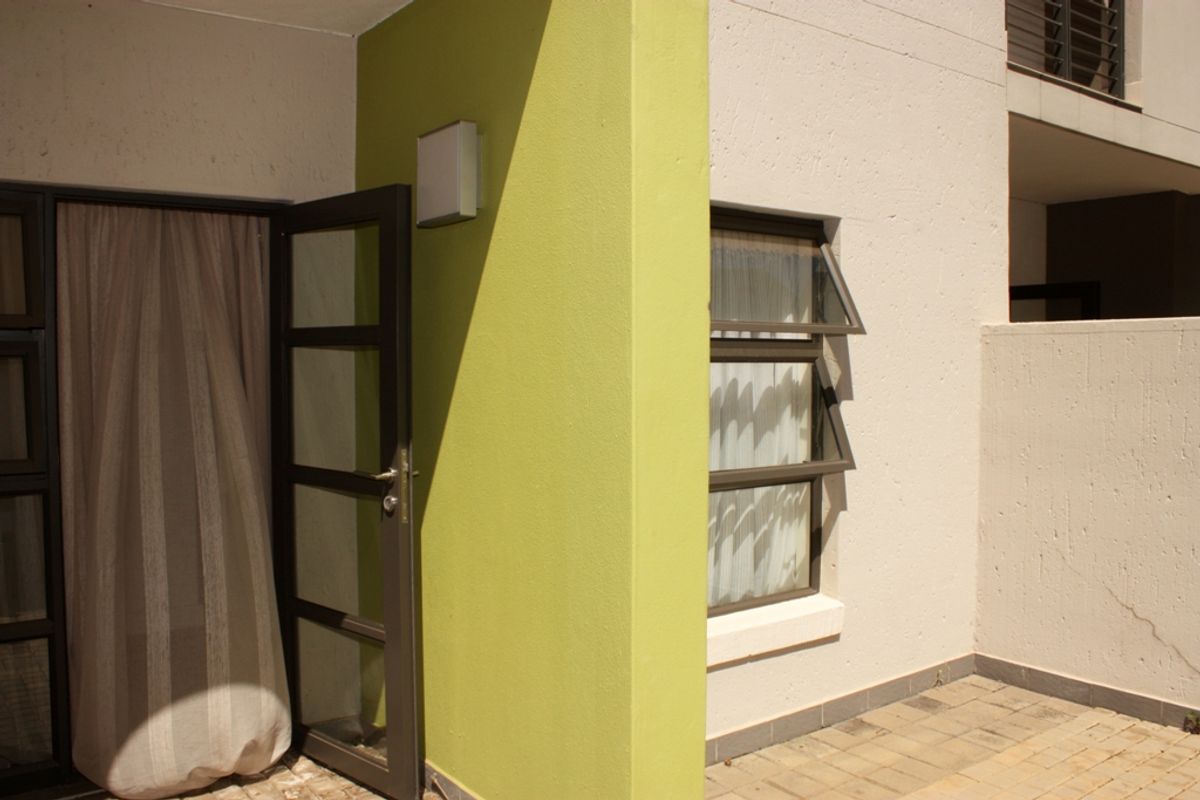 A view of the rear exterior area featuring a paved patio, aluminium window and door frames, and a lime green accent wall.