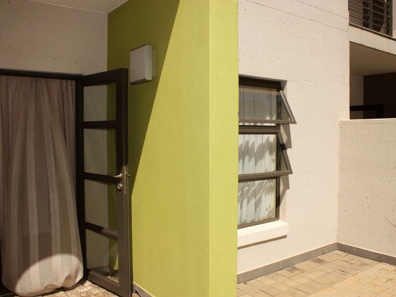 A view of the rear exterior area featuring a paved patio, aluminium window and door frames, and a lime green accent wall.