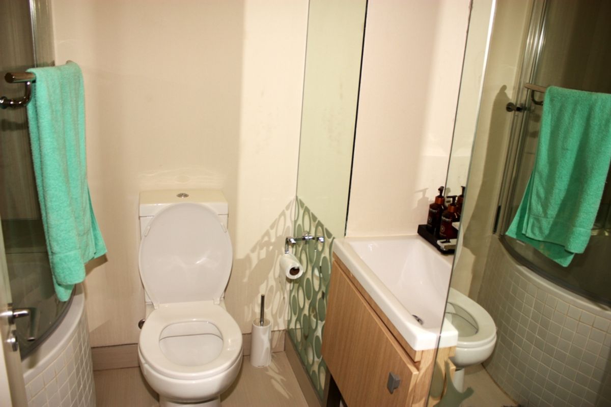 Compact bathroom featuring a toilet, vanity basin, and a glass-enclosed shower with tiled base.