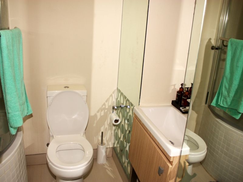 Compact bathroom featuring a toilet, vanity basin, and a glass-enclosed shower with tiled base.