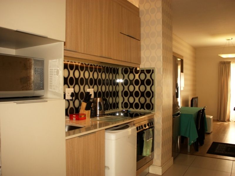 Open-plan kitchen featuring modern wood-finish cabinetry, integrated appliances, and a distinctive patterned splashback, flowing into a connected living and dining area.