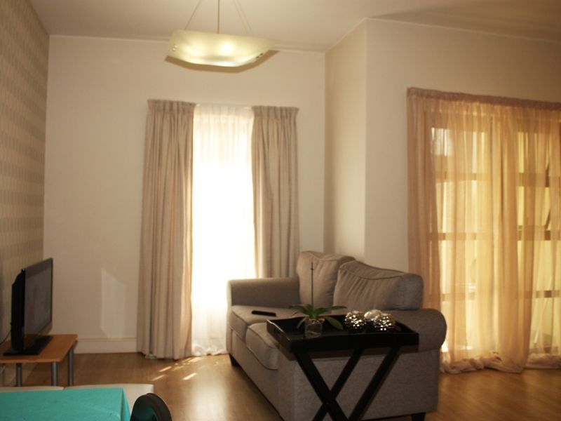 A living room featuring laminate flooring, neutral walls, and natural light through curtained windows and a glass door.