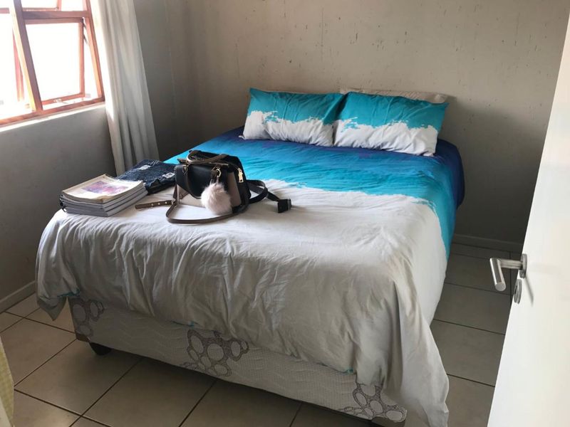 A bedroom featuring tiled flooring and a window, currently showing signs of wear on the wall surfaces.