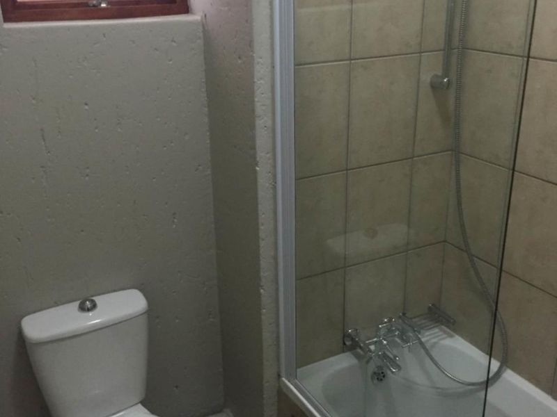 A functional bathroom featuring a combined bathtub and shower with a glass screen, a standard toilet, and tiled wall finishes.