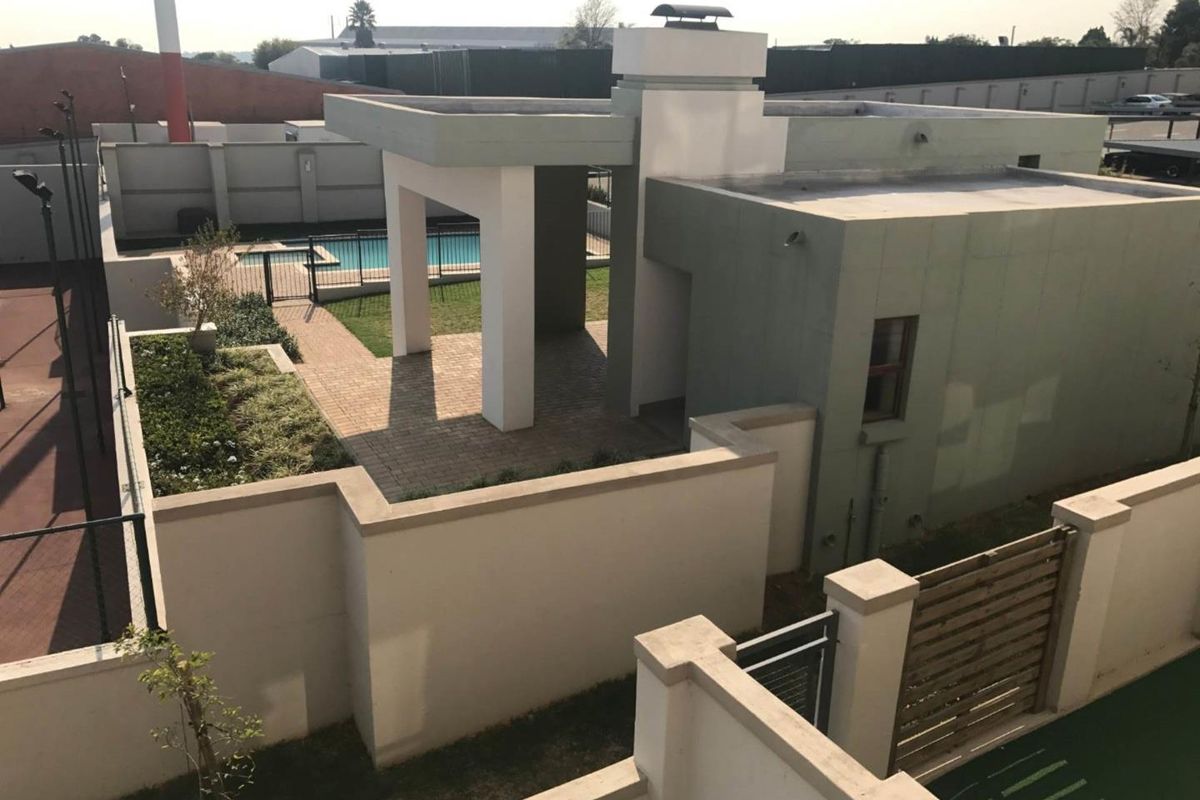 Aerial view of the apartment complex grounds featuring a swimming pool, covered patio area, and secure perimeter walls.