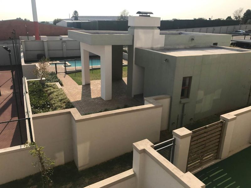 Aerial view of the apartment complex grounds featuring a swimming pool, covered patio area, and secure perimeter walls.