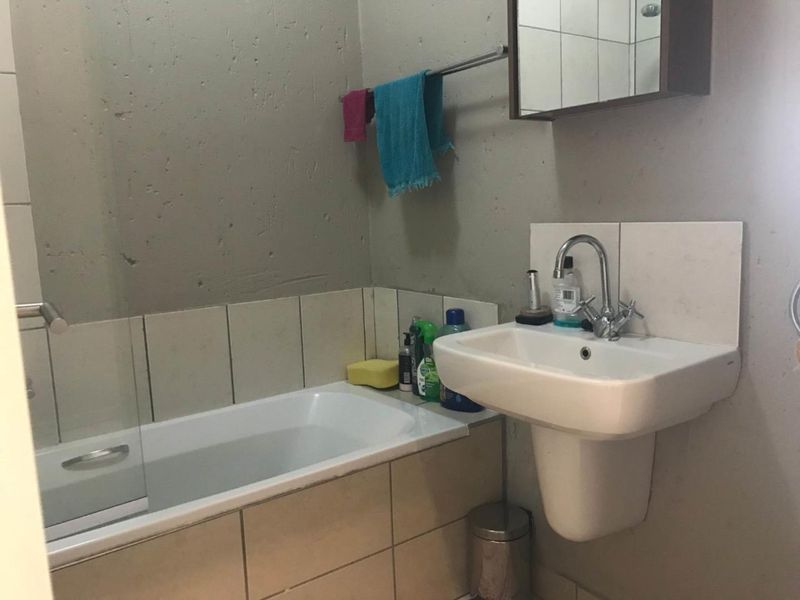 A compact bathroom featuring a pedestal washbasin, built-in bathtub with a glass screen, and wall-mounted storage, requiring cosmetic updates to the wall finishes.