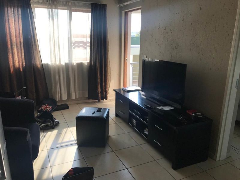 A living room area featuring tiled flooring, a large window, and access to an outdoor balcony through a sliding door.