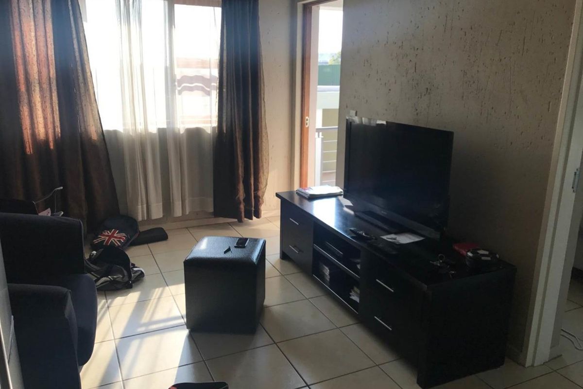 A living room area featuring tiled flooring, a large window, and access to an outdoor balcony through a sliding door.