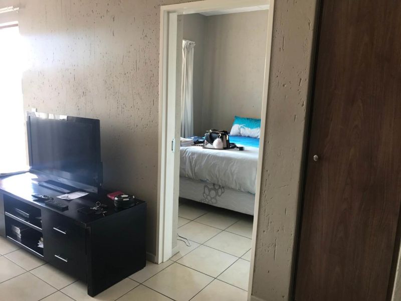 Living area with tiled flooring and a view into the adjacent bedroom, featuring a built-in cupboard and textured wall finishes.