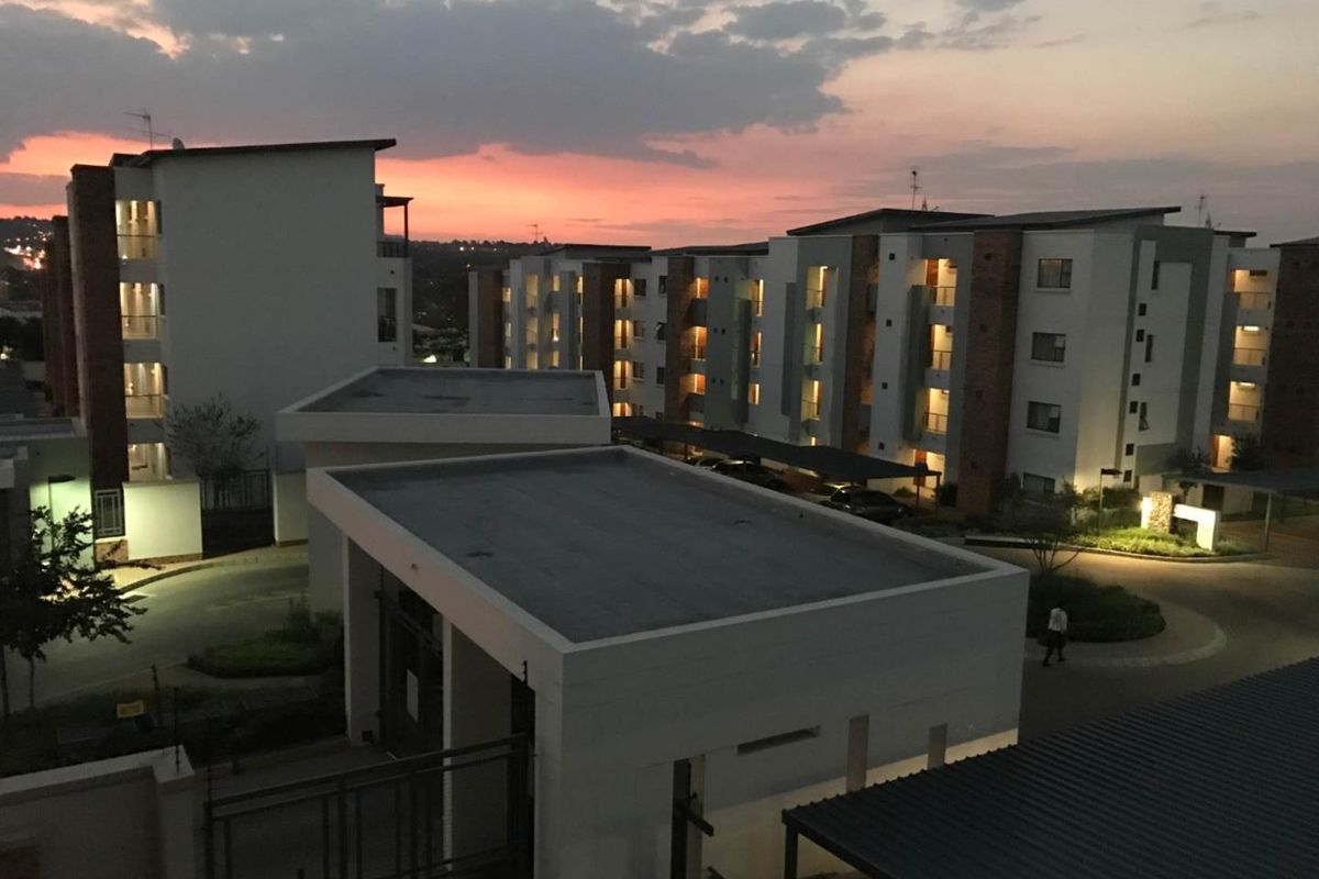 Elevated view of a modern apartment complex at sunset, featuring multi-story residential blocks, covered parking, and well-maintained communal grounds.