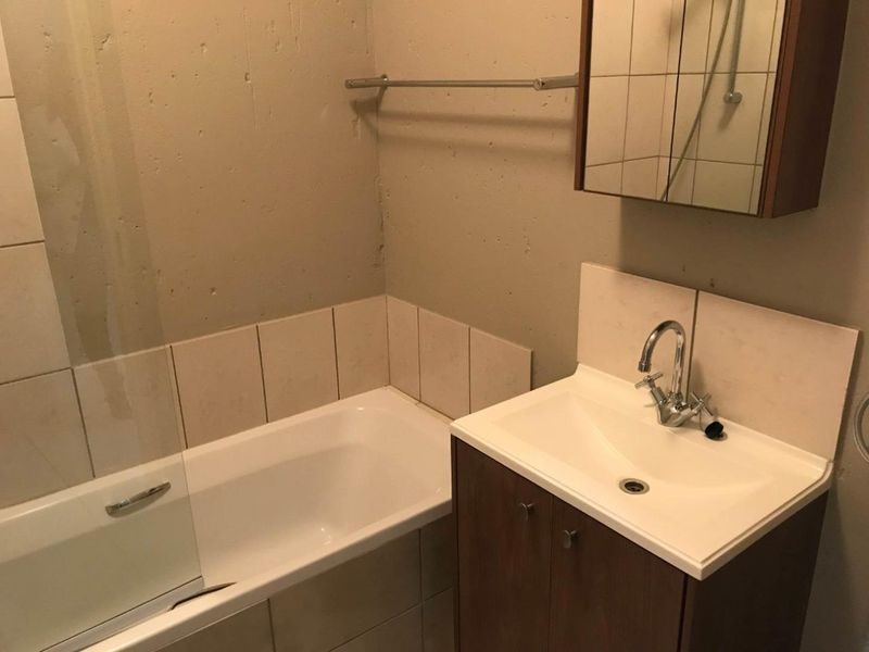 A functional bathroom featuring a built-in vanity with basin, a bathtub with a glass screen, and a mirrored medicine cabinet.