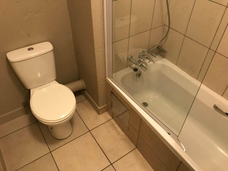 A functional bathroom featuring a standard toilet, a bathtub with a shower mixer, and a glass shower screen, finished with neutral floor and wall tiles.
