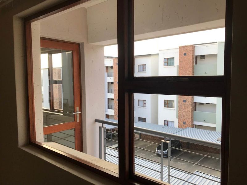 View from an interior window looking out towards the apartment complex courtyard, parking area, and adjacent building facade.