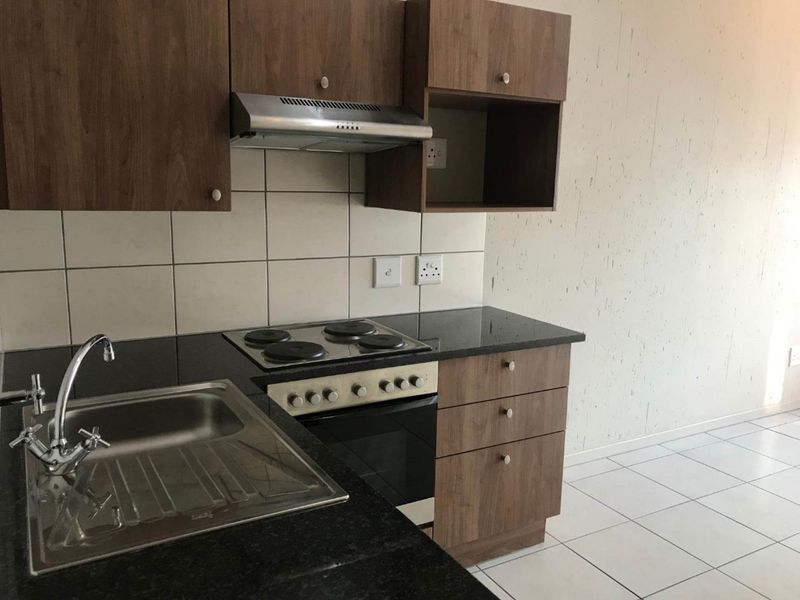 A compact kitchen featuring dark wood cabinetry, granite countertops, a built-in electric stove with extractor fan, and tiled flooring.