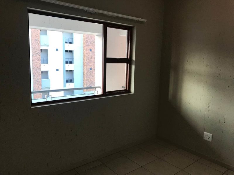 An empty bedroom featuring tiled flooring and an aluminium window frame, offering a blank canvas for interior design and personalization.
