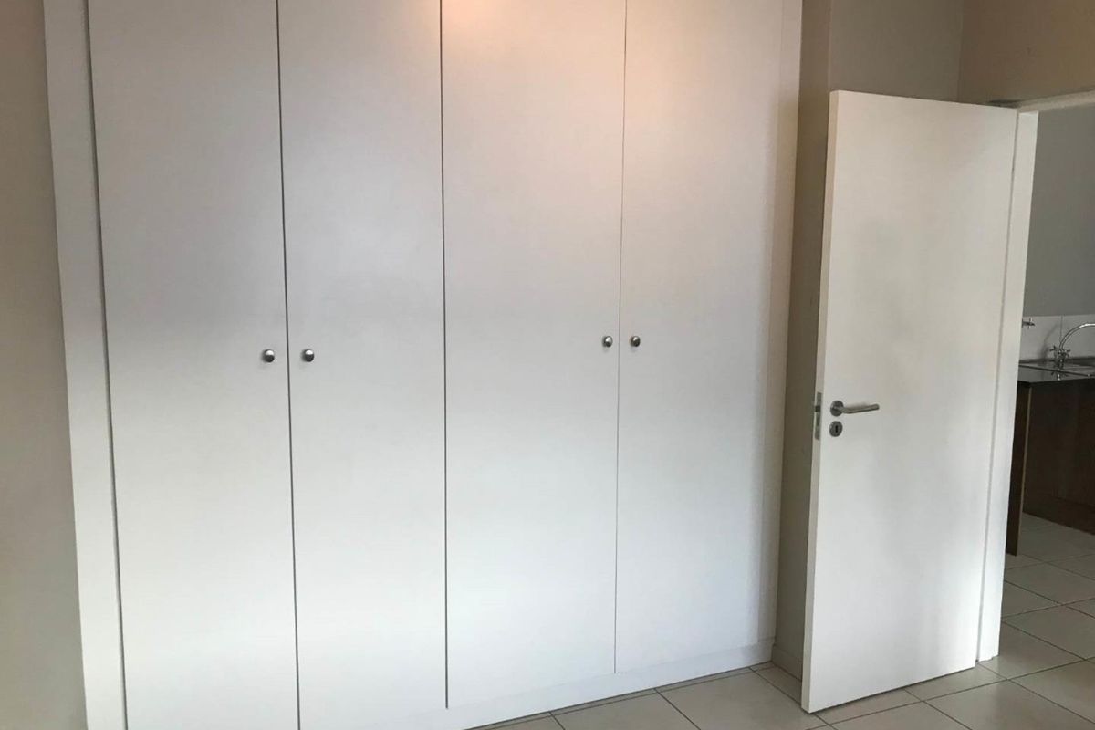 A clean, empty bedroom featuring neutral tiled flooring and ample built-in cupboard storage space.
