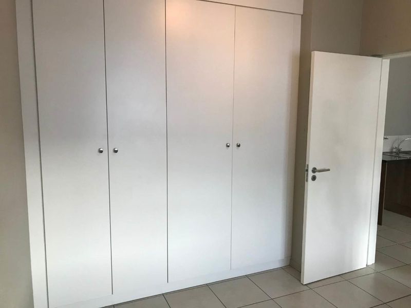 A clean, empty bedroom featuring neutral tiled flooring and ample built-in cupboard storage space.