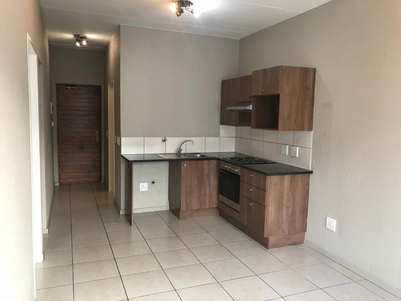Compact kitchen featuring laminate cabinetry, granite countertops, built-in oven, hob, and extractor fan, with tiled flooring and backsplash.