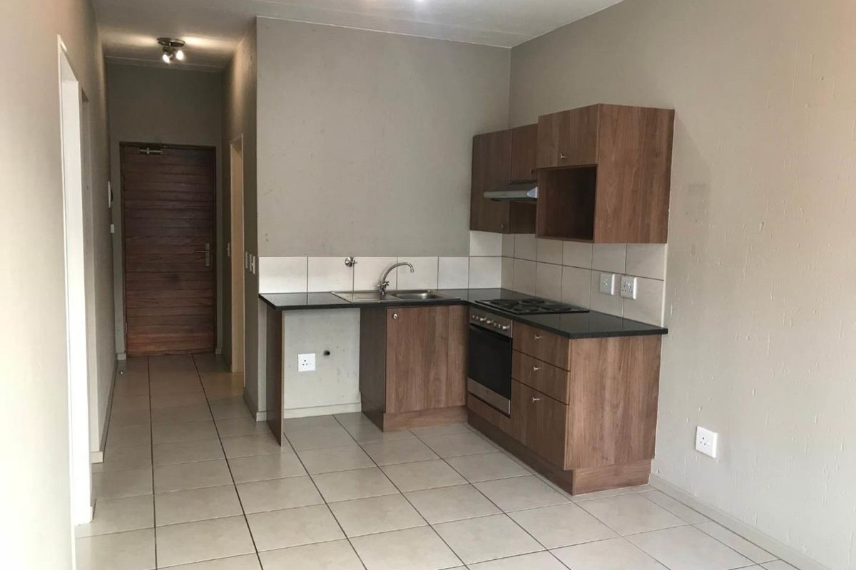Compact kitchen featuring laminate cabinetry, granite countertops, built-in oven, hob, and extractor fan, with tiled flooring and backsplash.