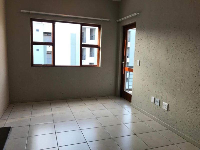 An empty living area featuring neutral tiled flooring, textured walls, and direct access to an outdoor balcony through a timber-framed door.
