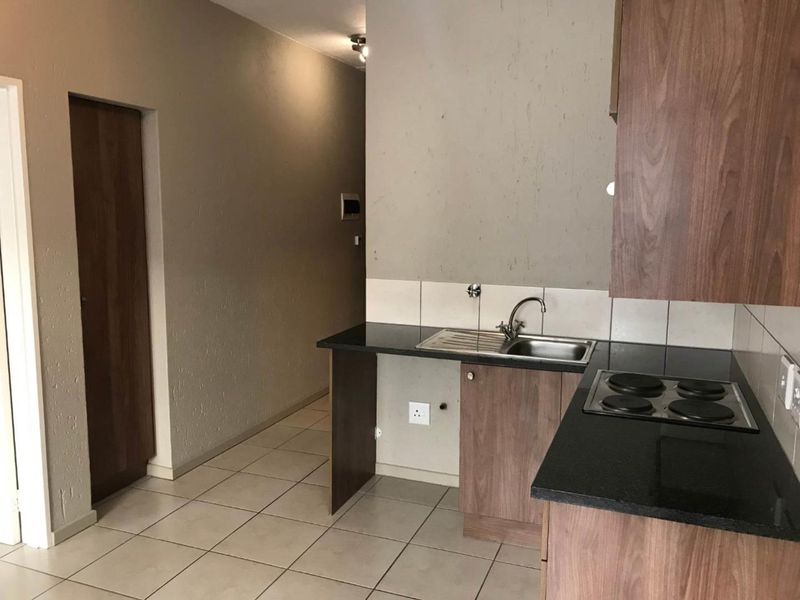 A compact kitchen featuring wood-finish cabinetry, a stainless steel sink, and an integrated electric hob with tiled splashbacks and dark countertops.