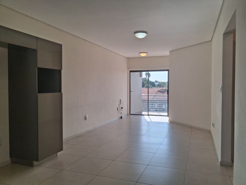 A bright, empty living area featuring neutral tiled flooring, built-in cabinetry, and a sliding glass door leading to an outdoor balcony.