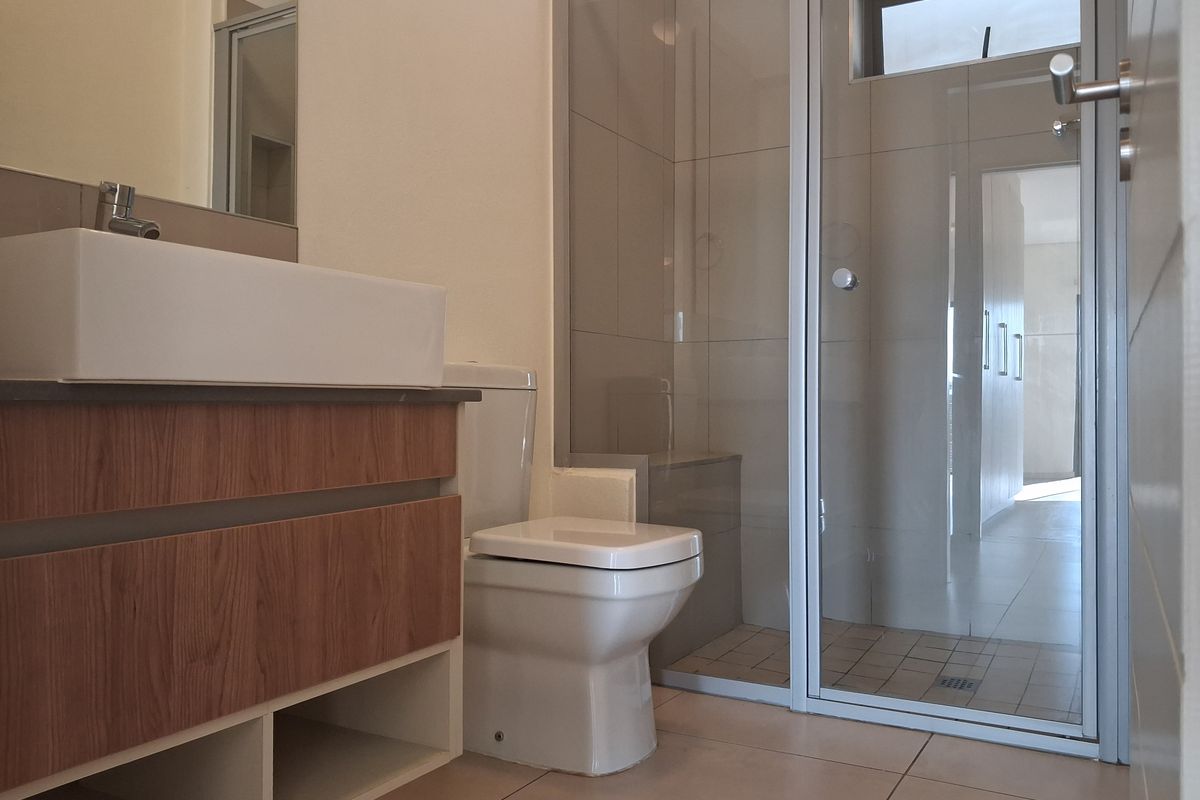 Modern bathroom featuring a floating wood-finish vanity, vessel sink, toilet, and a glass-enclosed shower with neutral wall and floor tiling.