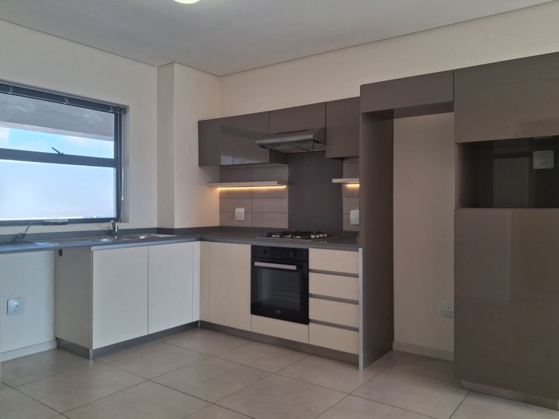 Modern kitchen featuring sleek two-tone cabinetry, built-in gas hob, electric oven, extractor fan, and tiled flooring in a clean, contemporary layout.