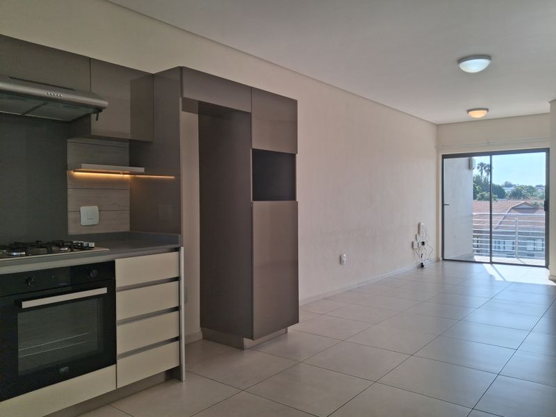 Modern open-plan kitchen and living area featuring sleek cabinetry, built-in appliances, tiled flooring, and direct access to a balcony through sliding glass doors.