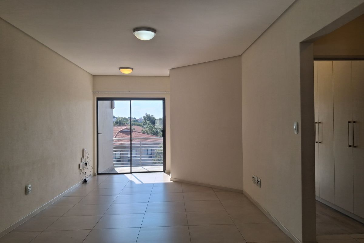 An empty, open-plan living area featuring neutral tiled flooring, built-in storage cupboards, and a sliding glass door leading to an outdoor balcony.