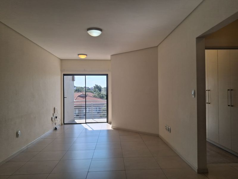 An empty, open-plan living area featuring neutral tiled flooring, built-in storage cupboards, and a sliding glass door leading to an outdoor balcony.