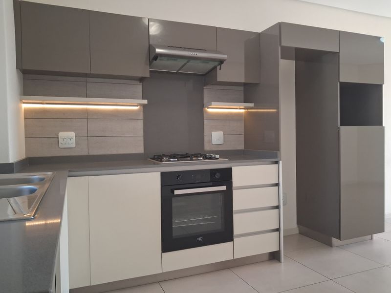 Modern kitchen featuring sleek grey and white cabinetry, stone countertops, built-in oven, gas hob, extractor fan, and integrated under-cabinet lighting.