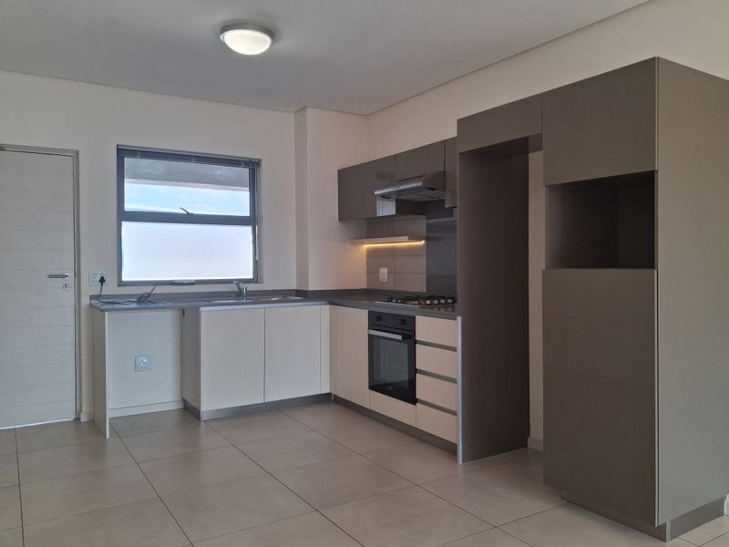 Modern kitchen featuring sleek two-tone cabinetry, built-in oven, gas hob, extractor fan, and tiled flooring in a clean, contemporary layout.