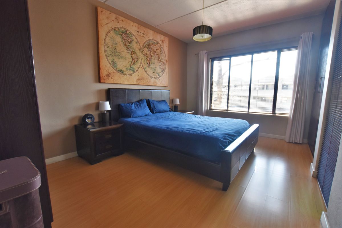 A well-lit bedroom featuring laminate flooring, built-in storage, and a large window that provides ample natural light.