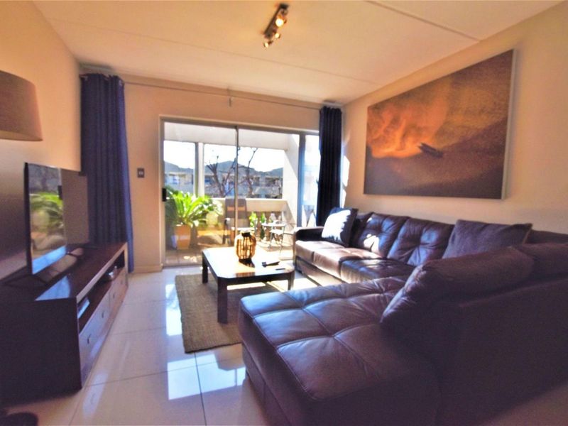 A comfortable living room featuring tiled flooring and a large sliding glass door that provides access to an outdoor balcony area.