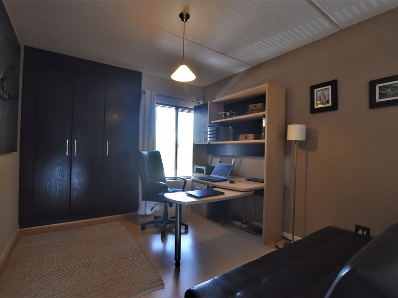 A functional home office featuring laminate flooring, built-in dark wood cupboards, and a dedicated workspace area with overhead pendant lighting.