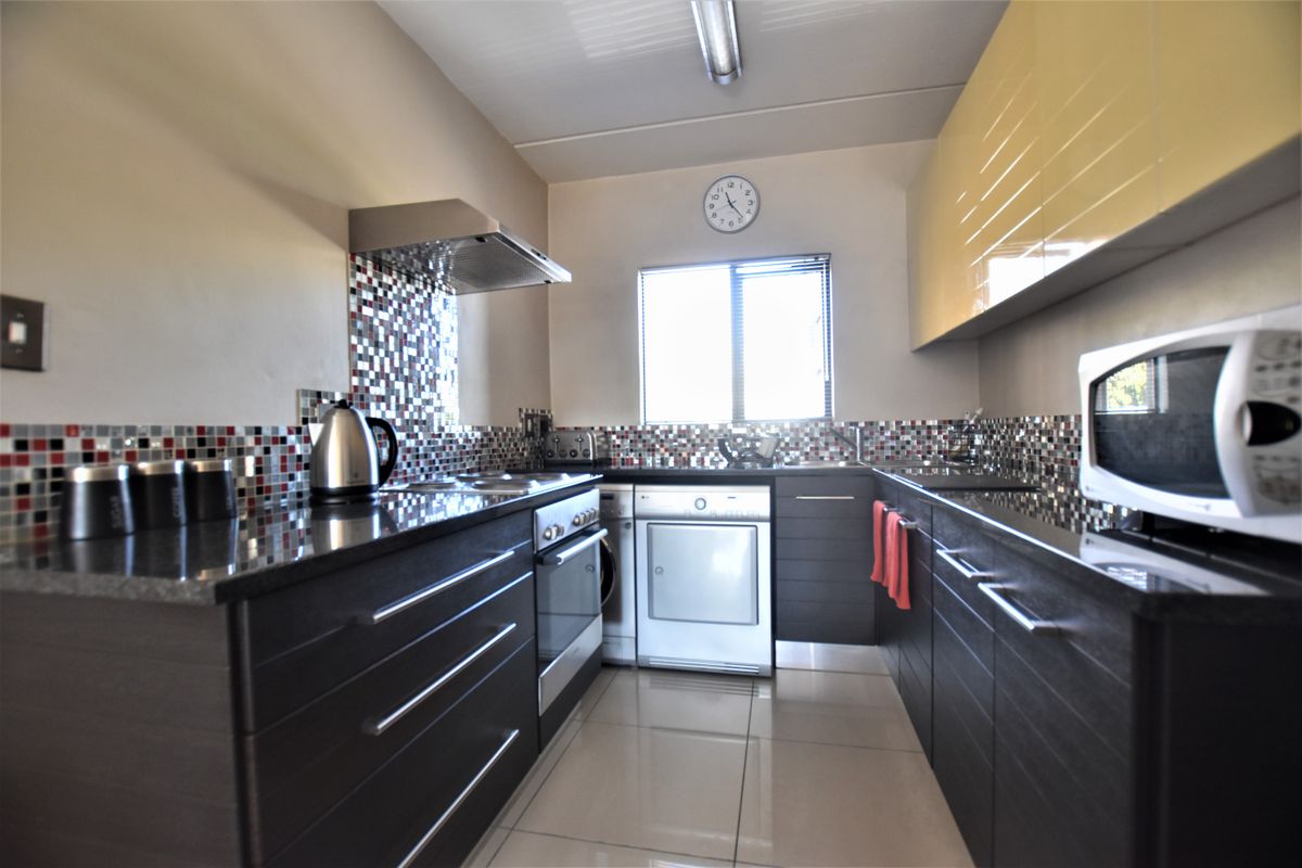 Modern galley-style kitchen featuring dark cabinetry, granite countertops, mosaic tile backsplash, and integrated stainless steel appliances.
