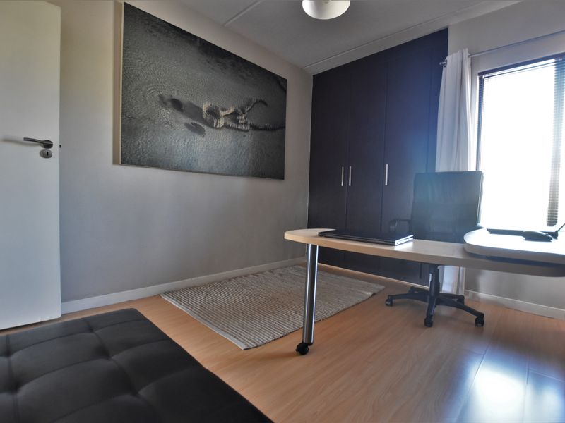 A functional home office featuring laminate flooring, built-in storage cupboards, and natural light through a window with fitted blinds.