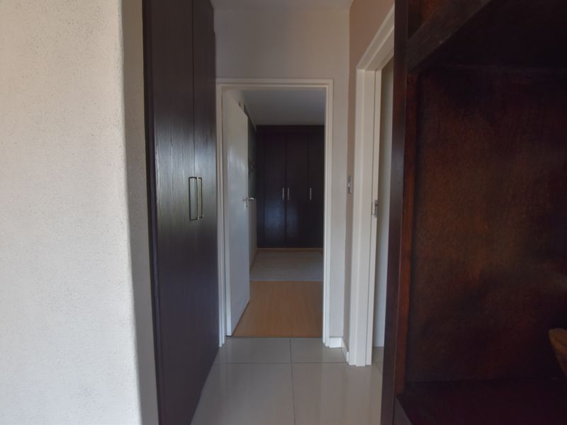 A functional hallway featuring built-in dark wood cupboards, connecting to an adjacent room with laminate flooring and additional storage.