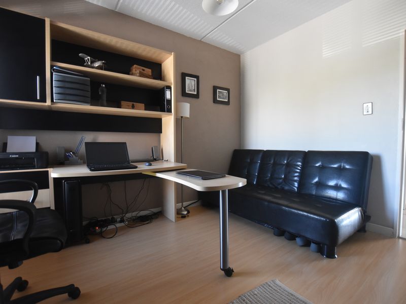 A functional home office space featuring a built-in desk and integrated shelving unit, finished with light-toned laminate flooring.