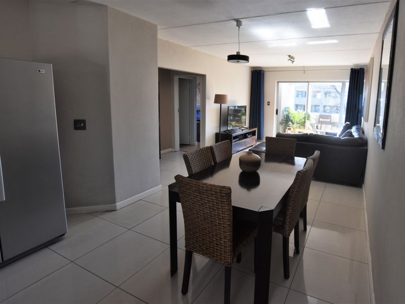An open-plan living and dining area featuring neutral tiled flooring, modern lighting, and a sliding glass door leading to an outdoor space.