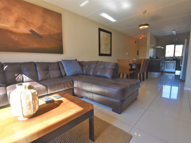 An open-plan living and dining area featuring polished tiled floors, recessed lighting, and a functional kitchen with built-in cabinetry and appliances.