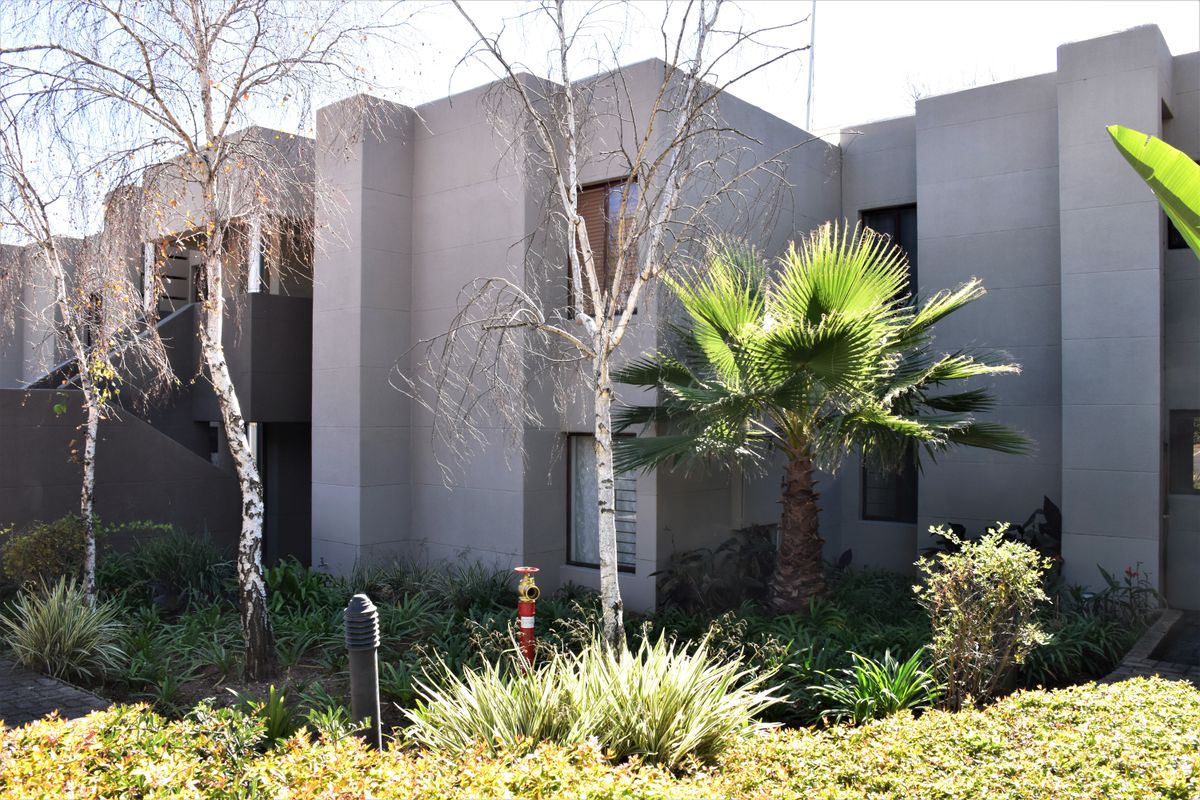 A view of the apartment building exterior featuring modern grey facade, landscaped garden area, and external staircase access.